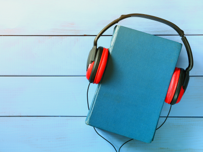 Blue book with orange headphones placed on it; link to Audiobooks page