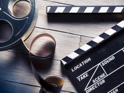 Movie film reel with unrolled film and open slate clapperboard; link to Movies page