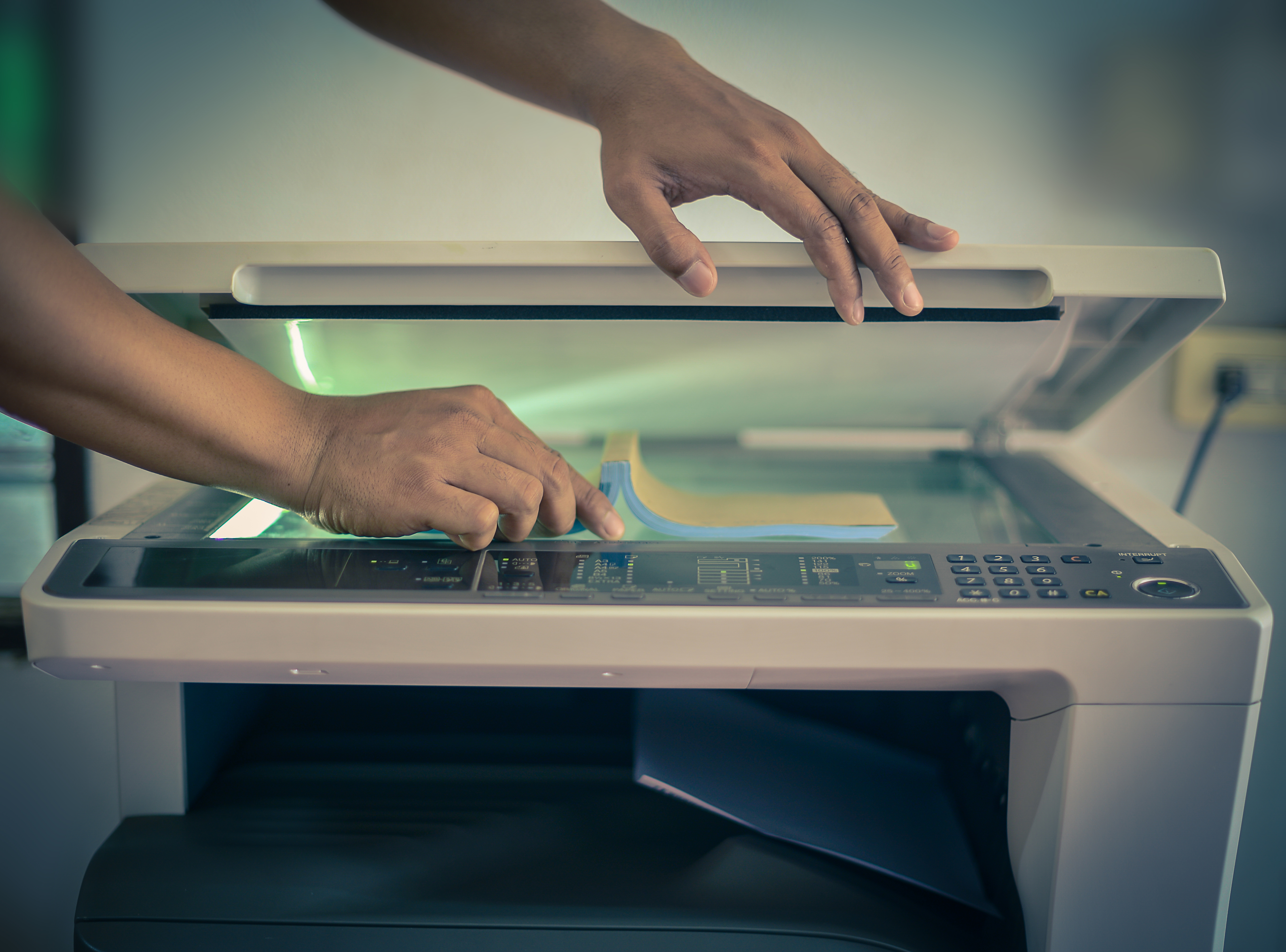 Hands placing paper on glass tray inside photocopier