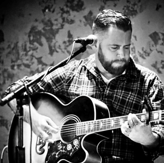 black and white photo of dan signor playing an acoustic guitar in front of a microphone