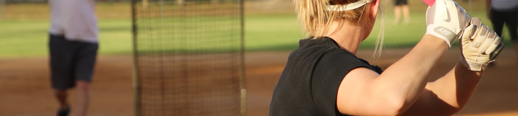 Softball field at Sunset, woman in the foreground with a bat about to swing
