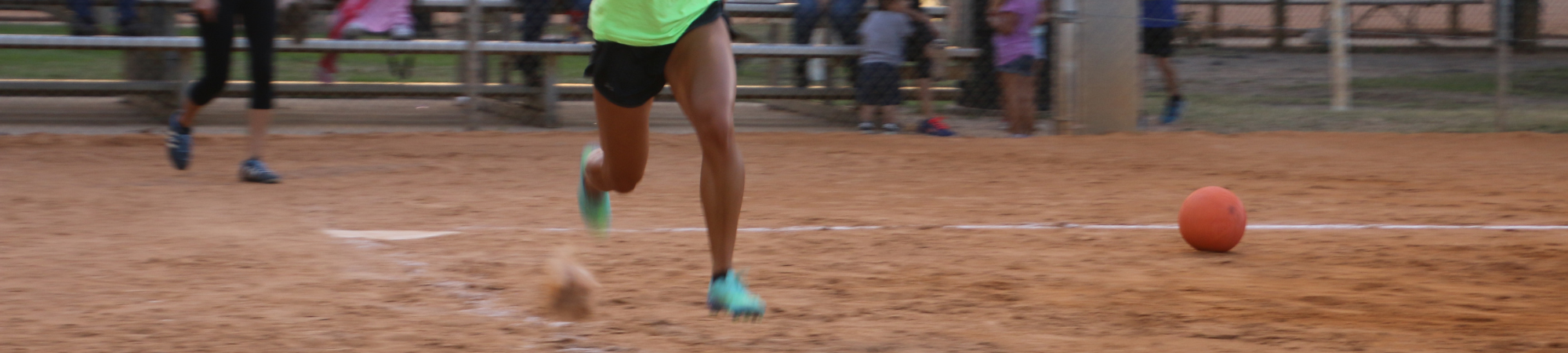 Woman running to first base with her ball in the field behind her.