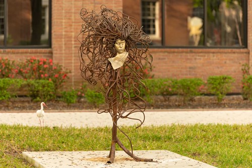 A women of gold with a neutral face and hair of bronze in a wlidly surrounding her