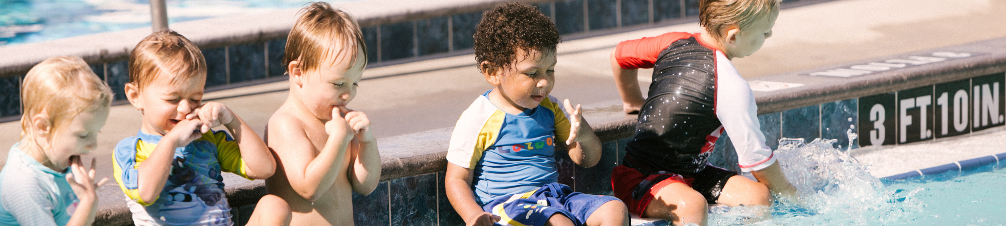 Five toddler age children sit on the side of the pool during a swim lessons