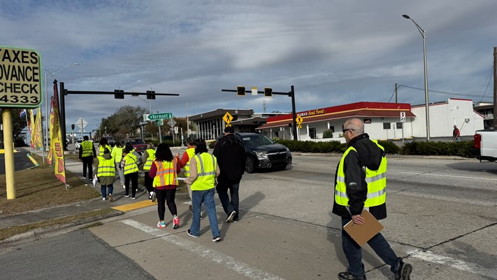 A group of people wearing yellow vests walking Memorial Blvd to conduct a walkability study.