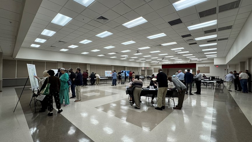 A public meeting with multiple tables. People are gathered at various tables speaking with organizers about the Memorial Blvd Study