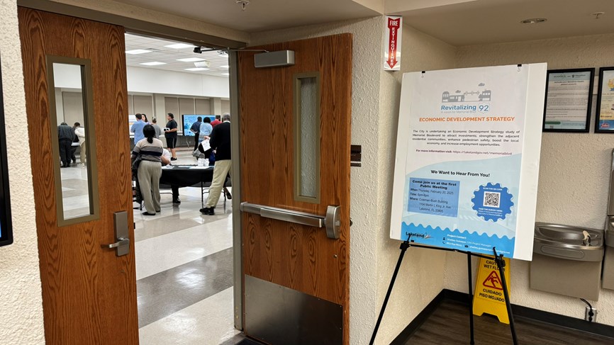 A picture of a sign and a door. The sign is about the Memorial Blvd Study, and there is a public meeting happening just past the pictured doors.