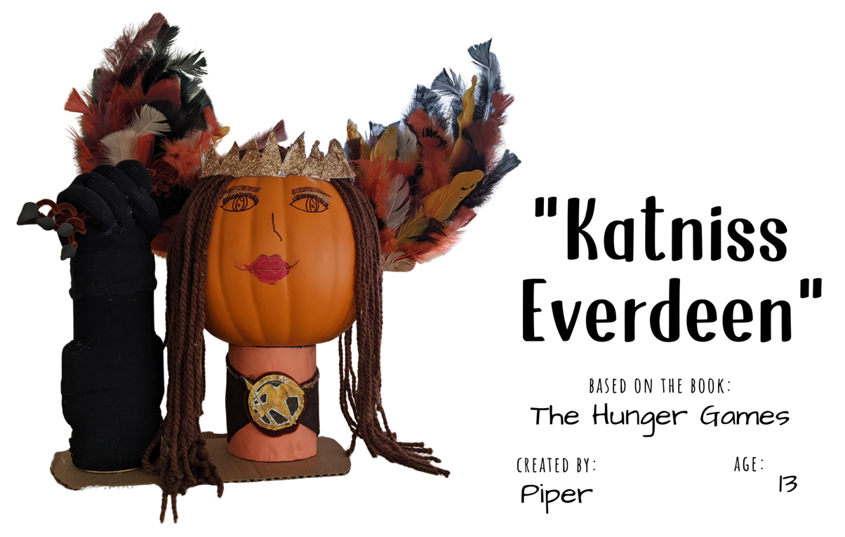Craft pumpkin painted to look like a smiling woman wearing a large feathered headpiece and golden crown with text "Katniss Everdeen; Based on the book The Hunger Games; Created by: Piper, Age 13"