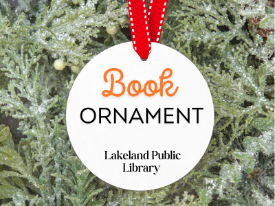 White ornament on evergreen branches background with text Book Ornament, Lakeland Public Library