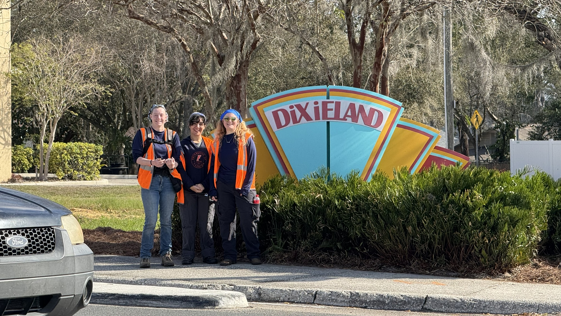 Three surveyors in orange visibility vests standing next to a sign that says "Dixieland."