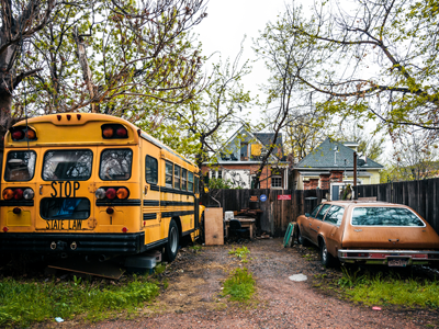 An old yellow school bus, a derelict vehicle and other code violations in the yard of a house.