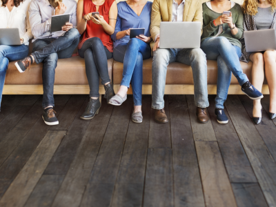 Group of people seated on bench using laptops and electronic devices