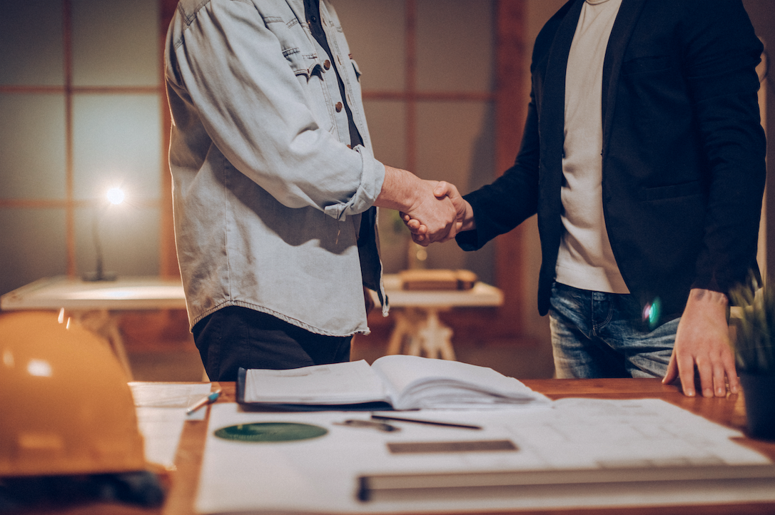 two men shaking hands in a business deal over a busy desk